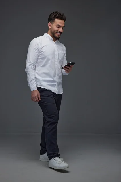 Saudi Man Walking While Using Smartphone in Grey Studio