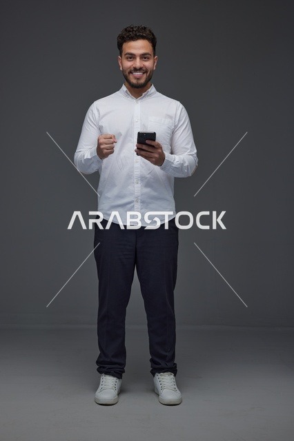 رجل سعودي مبتسم مع هاتف ذكي وإيماءة نجاح