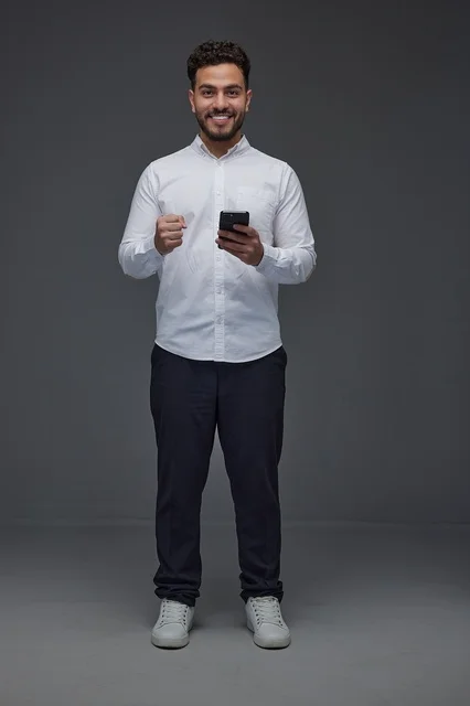 Smiling Saudi Man with Smartphone Success Gesture
