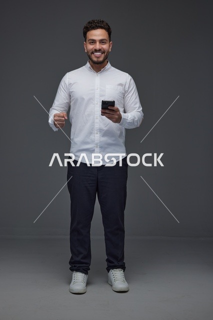 رجل سعودي مبتسم يستخدم الهاتف الذكي بخلفية رمادية