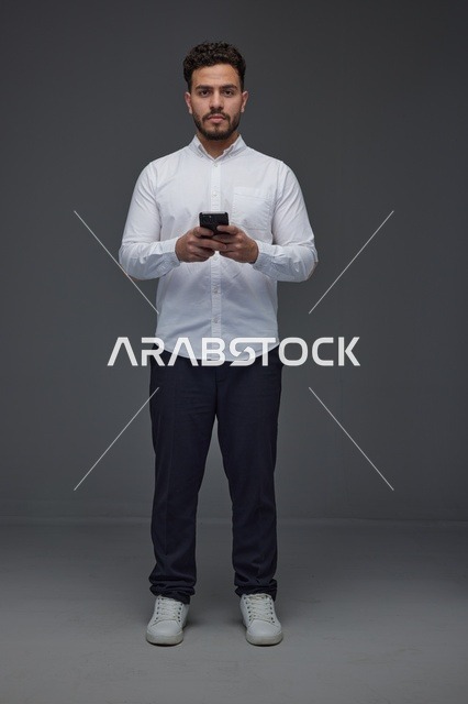 رجل سعودي يحمل هاتف ذكي في استوديو بخلفية رمادية