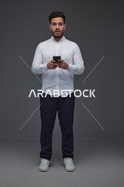 رجل سعودي يستخدم الهاتف الذكي بتعبير متفاجئ