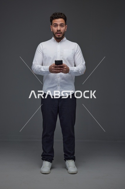رجل سعودي يستخدم الهاتف الذكي بتعبير متفاجئ