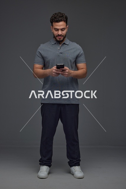 رجل سعودي يستخدم الهاتف الذكي بخلفية رمادية داخل الاستوديو