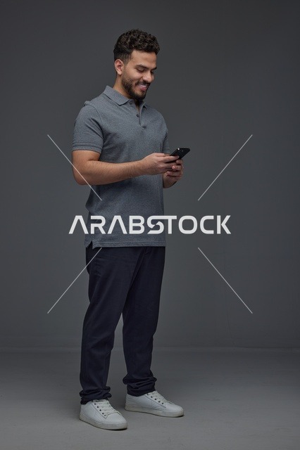 رجل سعودي يستخدم الهاتف الذكي بخلفية استوديو رمادية