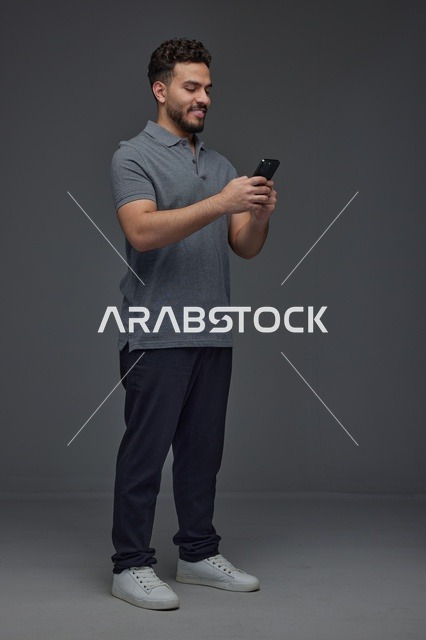 رجل سعودي يستخدم الهاتف الذكي في استوديو رمادي