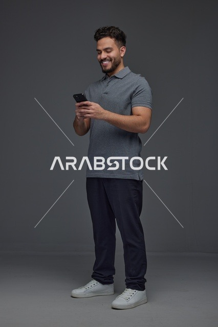 رجل سعودي يستخدم الهاتف الذكي في استوديو رمادي