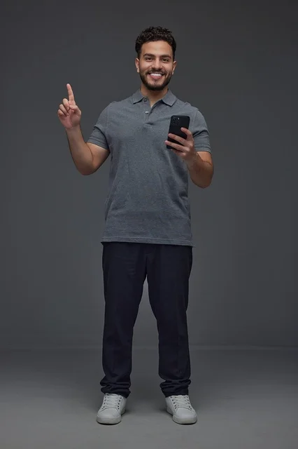 Saudi Man Holding Smartphone and Pointing Up in Studio
