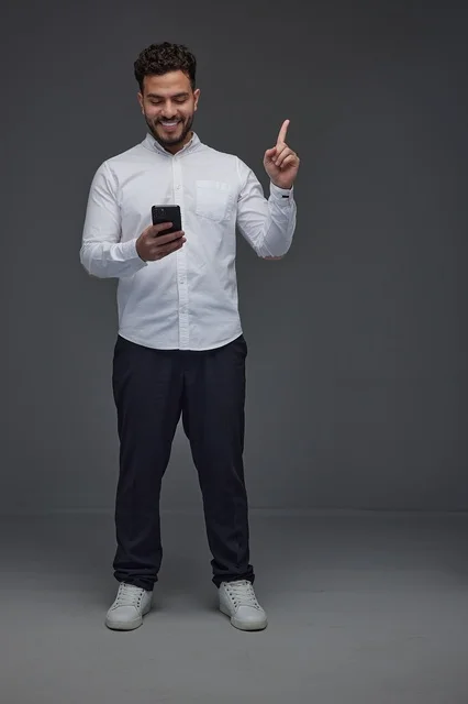 Saudi Man with Smartphone Pointing Up on Grey Background