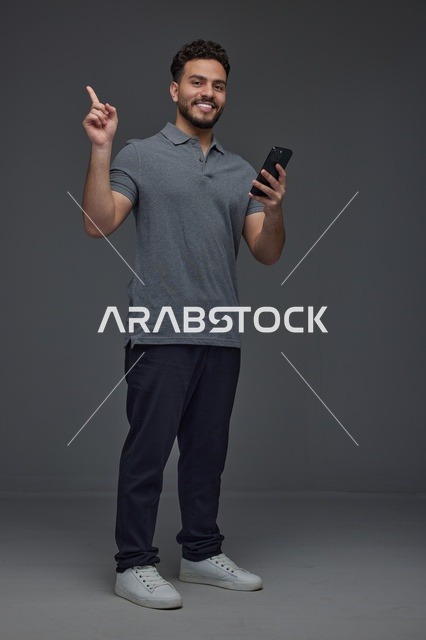 رجل سعودي يحمل هاتف ذكي ويشير للأعلى في استوديو