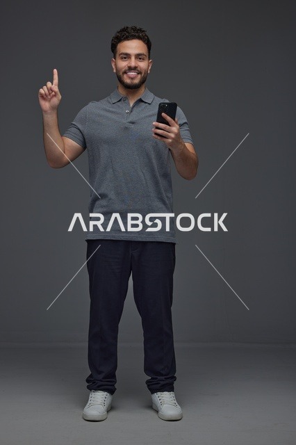 رجل سعودي يحمل هاتف ذكي ويشير للأعلى في استوديو