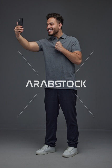 رجل سعودي مبتسم يلتقط صورة سيلفي بالهاتف الذكي في استوديو