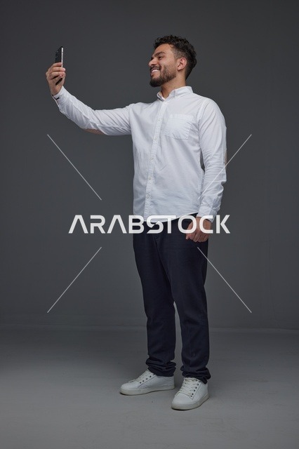 رجل سعودي يلتقط صورة سيلفي بالهاتف في استوديو رمادي