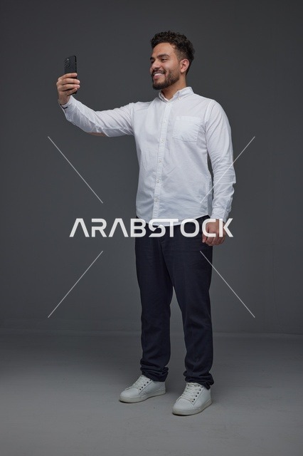 رجل سعودي مبتسم يلتقط صورة سيلفي بالهاتف الذكي في استوديو