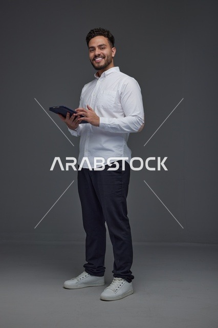 رجل سعودي يحمل جهازاً لوحياً رقمياً في استوديو احترافي