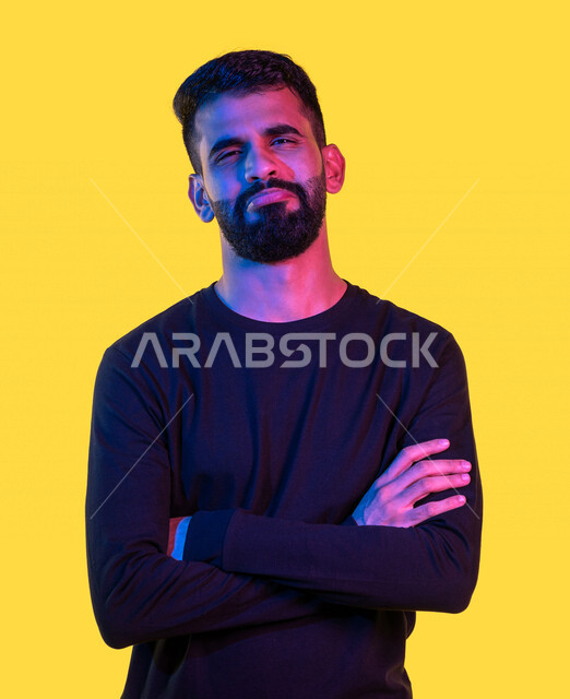 بورتريه لشاب عربي خليجي سعودي ينظر إلى الكاميرا ، متكتف اليدين بإيماءات و تعابير وجه و يدين تدل على العبوس و الحزن و الملل ، خلفية صفراء