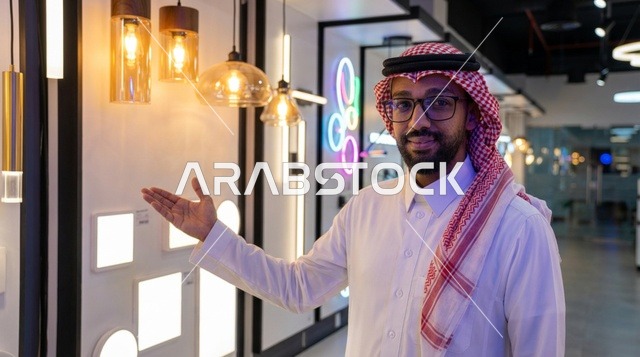 رجل سعودي يشير إلى مجموعة مصابيح في معرض إضاءة حديث