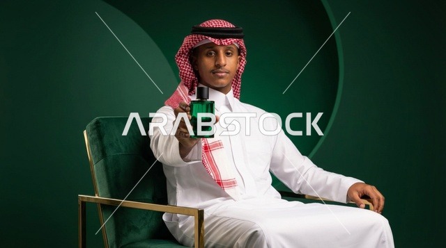 رجل سعودي يحمل زجاجة عطر في استوديو أخضر