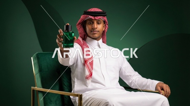 رجل سعودي مع زجاجة عطر في استوديو أخضر