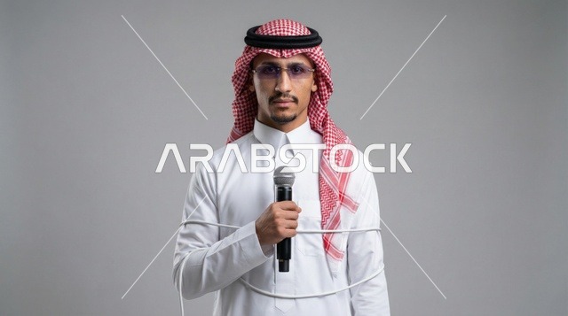 رجل سعودي يمسك ميكروفون مع سلك ملفوف في الاستوديو
