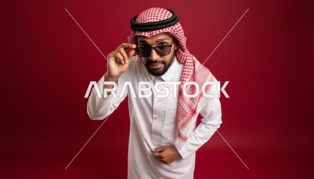 رجل سعودي بالثوب التقليدي والنظارات الشمسية خلفية حمراء