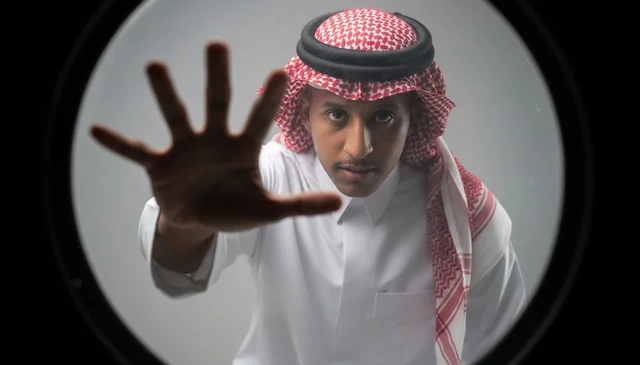 رجل سعودي بالزي التقليدي يمد يده للكاميرا
