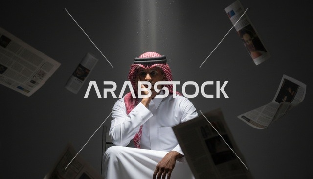رجل سعودي مع صحف متساقطة تحت الضوء