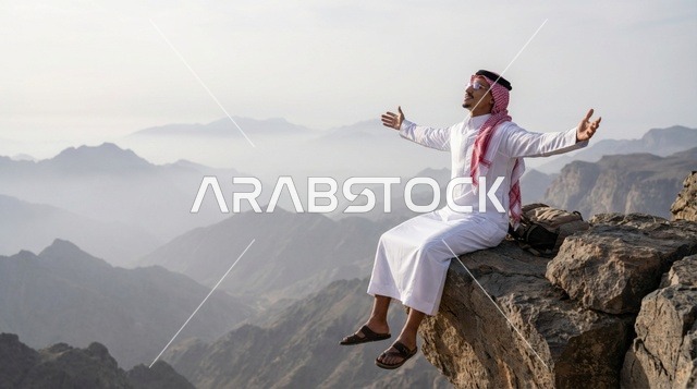 رجل سعودي يجلس على حافة جبل بذراعين مفتوحتين