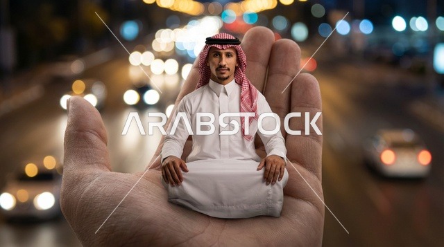 رجل سعودي بالثوب التقليدي يجلس على يد عملاقة ليلاً