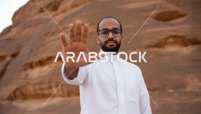 رجل سعودي بالثوب الأبيض يشير بالتوقف في الصحراء