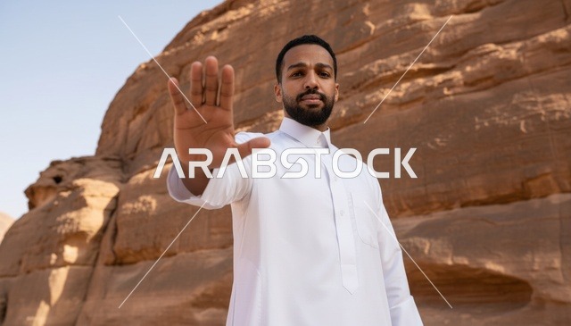 رجل سعودي بالثوب الأبيض يشير بعلامة التوقف في الصحراء