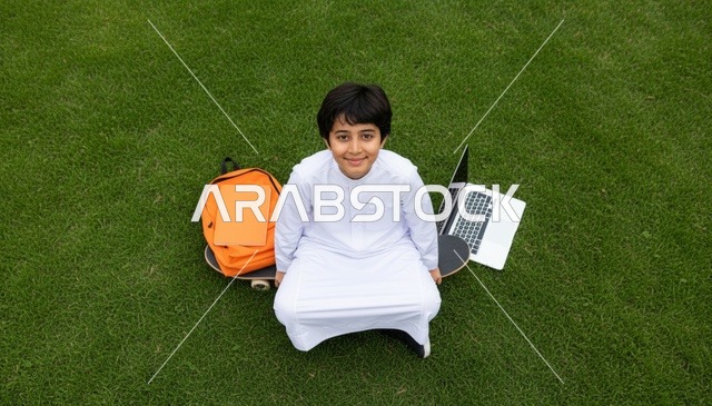 طفل عربي بالثوب الأبيض مع حاسوب في الحديقة