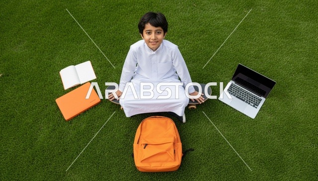 طالب سعودي بالثوب مع حاسوب على عشب أخضر