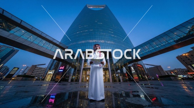 رجل سعودي أمام برج المملكة في الرياض ليلاً