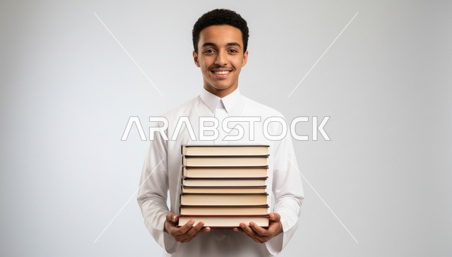 شاب سعودي يرتدي الثوب الأبيض ويحمل مجموعة من الكتب