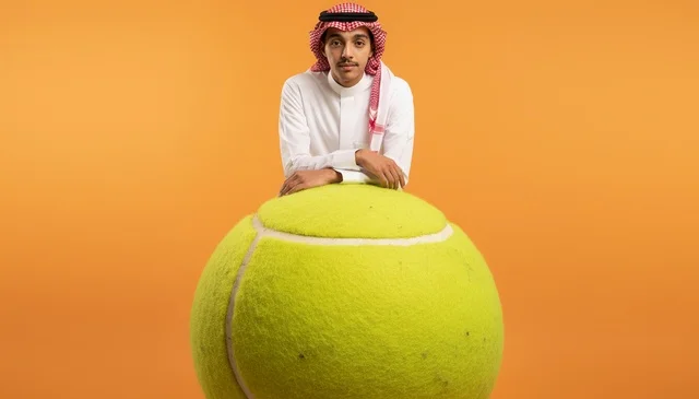 رجل سعودي يرتدي الزي التقليدي يستند على كرة جولف