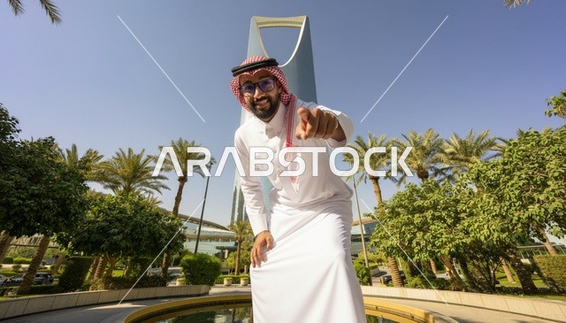 رجل سعودي أمام برج المملكة بالرياض يشير نحو الكاميرا