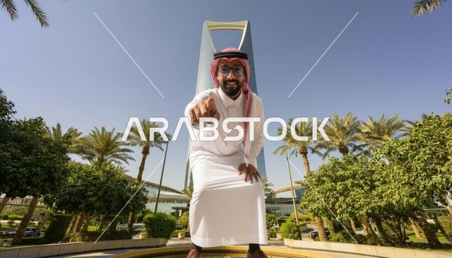 رجل سعودي عند برج المملكة بالرياض يشير للكاميرا