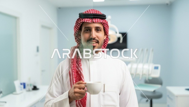 رجل سعودي بالزي التقليدي يحمل كوباً في عيادة أسنان