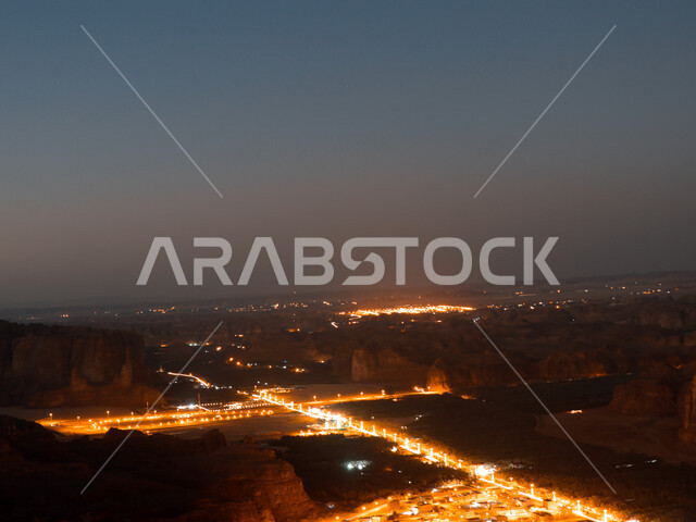 صورة إبداعية ليلية لقرية العلا التراثية شمال غرب المملكة العربية السعودية ، منظر علوي لمدينة العُلا والجبال المحيطة بها مضاءة ليلاً ، أماكن سياحية في السعودية ، المعالم التاريخية والآثرية القديمة في بلدة العلا القديمة ، الحضارة العربية القديمة