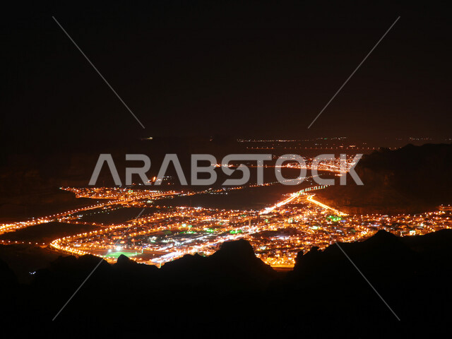 صورة إبداعية ليلية لقرية العلا التراثية شمال غرب المملكة العربية السعودية ، منظر علوي لمدينة العُلا والجبال المحيطة بها مضاءة ليلاً ، أماكن سياحية في السعودية ، المعالم التاريخية والآثرية القديمة في بلدة العلا القديمة ، الحضارة العربية القديمة