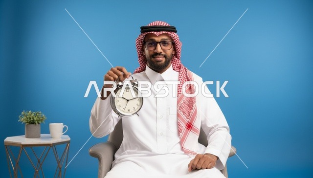 رجل سعودي بالزي التقليدي يمسك ساعة منبه