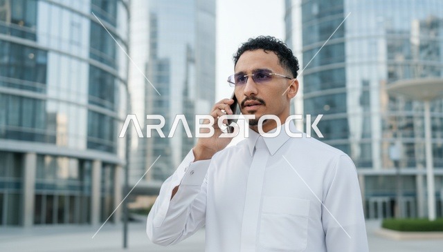 رجل سعودي بالثوب يتحدث بالهاتف في منطقة أعمال حديثة