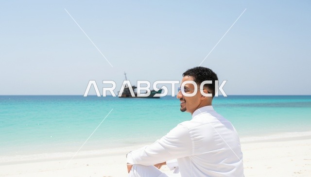 رجل سعودي على الشاطئ مع إطلالة سفينة محطمة