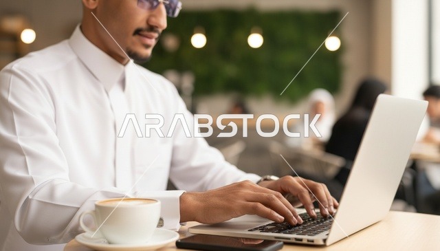 رجل سعودي بالثوب الأبيض يعمل على الكمبيوتر في مقهى