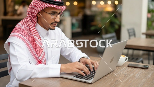 رجل سعودي يعمل على جهاز محمول في مقهى خارجي