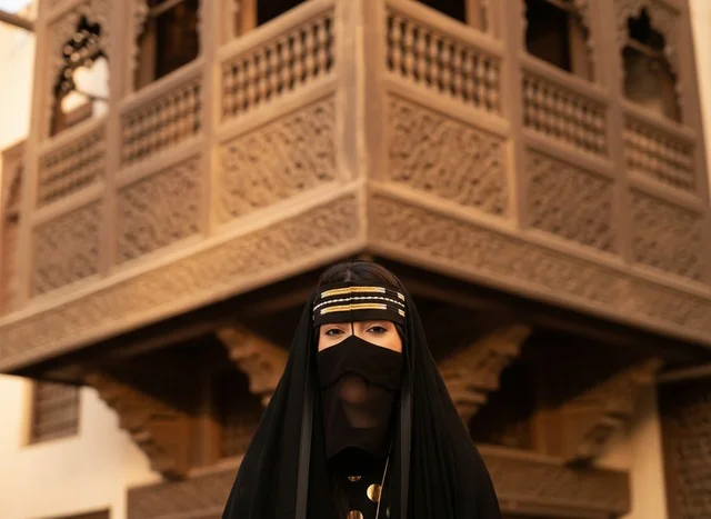 امرأة سعودية بالزي التقليدي أمام مشربية قديمة