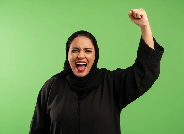 امرأة إماراتية بالعباءة في وضعية نصر خلفية خضراء