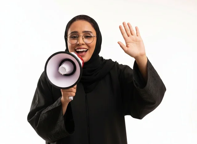 امرأة سعودية بالعباءة تمسك مكبر صوت بخلفية بيضاء
