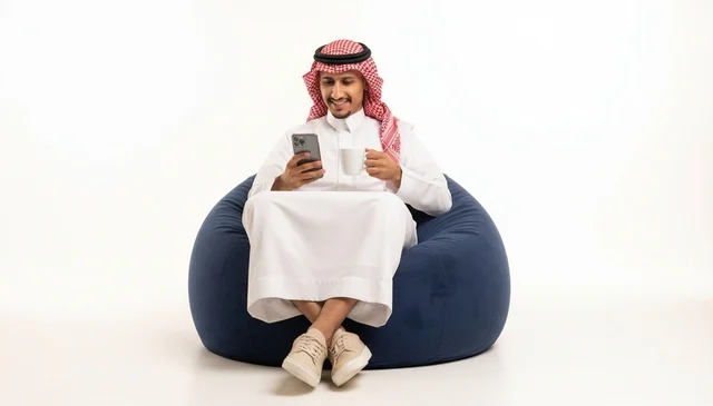 رجل سعودي بالزي التقليدي يستخدم الهاتف على كنبة استرخاء